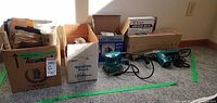 Two Makita sanders with boxes of sanding supplies on carpeted floor