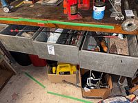Workbench with open metal drawers showing hand tools, clamps, bottle jack, yellow tool case