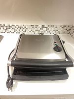 Closed Breville panini press showing stainless lid, handle and power cord