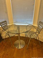 Round glass table with two metal slat armchairs in bay window setting