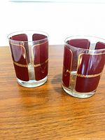 Pair of burgundy and gold trimmed old fashioned glasses on wood surface
