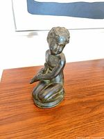 Full view of patinated clay kneeling cherub figurine on wooden surface