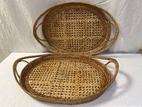 Both oval woven rattan trays, one standing upright, one lying flat