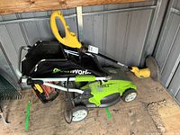 Greenworks lawn mower with grass bag and extension cord, Weed Eater trimmer resting on top