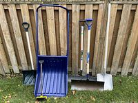 all five snow-removal tools lined against fence