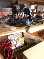 Shelf with multiple corded tools, red cables, drill bit case