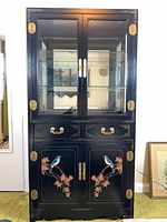 Front view of black chinoiserie cabinet showing glass display top, drawers, painted lower doors