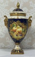 Front view showing hand-painted fruit scene, cobalt blue ground, gilt handles and finial