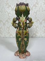 Full view of footed majolica-style ceramic vase showing thistle relief and glazing