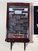 Front view showing glass door, carved top and bottom, metal support brackets