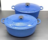 Two blue Le Creuset Dutch ovens with lids