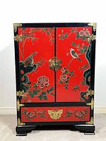 Front view of red lacquer cabinet closed showing painted motifs and brass hardware