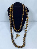 Two tiger's eye bead necklaces displayed on bust with brooch beneath