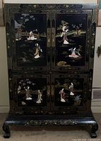 Front view showing closed doors with inlaid scenes and brass hardware