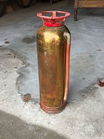 Front view brass antique fire extinguisher showing red wheel, hose, patina
