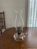 Glass oil lamp on table showing body, burner, chimney