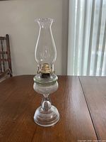 Full view of clear glass oil lamp showing chimney, burner, reservoir, stem and base