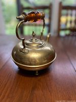 Side view showing brass kettle, amber handle, spout, feet
