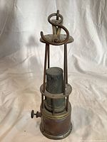 Full view of brass miner's lamp front, showing base, rods, gauze and hook