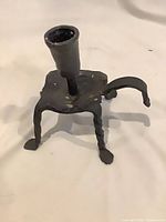 Front view showing three twisted legs, square plate, candle cup, and loop handle