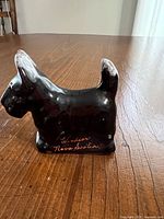 Left side view of black glazed Scottie dog figurine showing inscription 'Windsor Nova Scotia'.