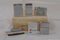 Front view of six lighters displayed on wooden block showing designs and logos