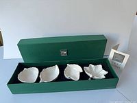 Closed green presentation box containing four white ceramic leaf dishes with leaflet visible