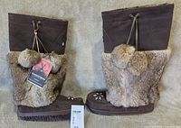 Side view of both boots showing suede uppers, fur shafts, beadwork, pom-poms, and hang tag