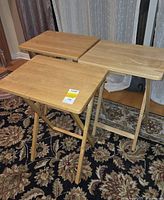 Three light wood folding TV tray tables standing open on patterned rug