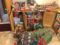 Overall lot view with cabinet showing wrapping paper rolls, gift bags, bows, artificial tree in green bag, wreaths and floral picks