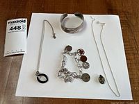 All five jewellery pieces laid out: charm bracelet, cuff, locket, two necklaces