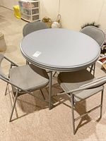 Round grey folding card table with four matching folding chairs