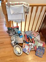 Overall lot view showing tablecloths on banister, pile of linens, doilies, silver-plate dishes, candles and napkins