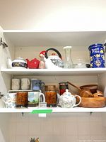 Cabinet shelves with teapots, kettle, Tetley tin, glass carafe, wooden salad set, mugs