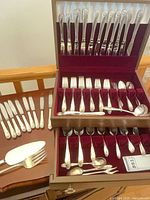 Two-tier wooden storage chest open displaying full set of flatware