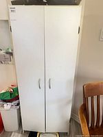 Front view of white two-door cupboard, oak chair partial