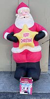 Full view of assembled inflatable Santa holding yellow star, retail box at base