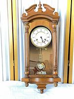 Full view of Emperor wall clock showing entire wood case, dial, glass door and pendulum
