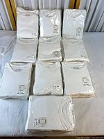 Ten sealed packs of white baby bodysuits arranged on table