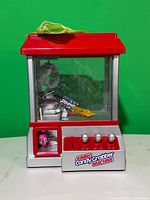 Front view of red and silver tabletop claw machine showing controls, clear case, and included candy