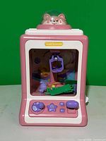 Front view of pink claw machine showing controls, window and internal claw