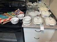 Group of CorningWare casseroles, ramekins and cookbooks on countertop