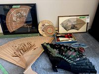 Overview of lot showing framed blossom fan, carved wood fan, straw fan, black floral fan, box of folding fans
