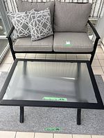 Loveseat with cushions and pillows beside glass-top coffee table on rug