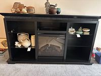 front view of black stand showing fireplace insert, shelves, contents not included