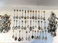 overview of entire assortment of souvenir teaspoons laid out and clustered, showing quantity and decorative variety