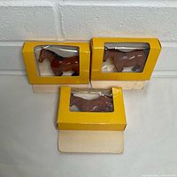 Three boxed Bullyland horse figurines, two upright, one lying, showing packaging and figures