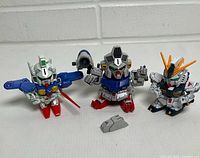 Front view of three SD Gundam figures and loose armor part