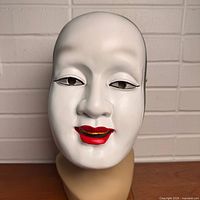 Front view of white resin Noh mask with red lips and black edging