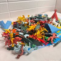 Pile of mixed plastic figures, horses, teepee, canoe on playmat